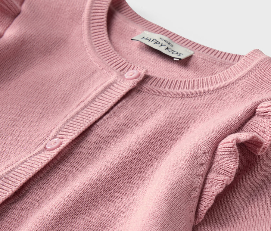 Detailaufnahme einer Kinder-Strickjacke in Rosa mit Rüschen.