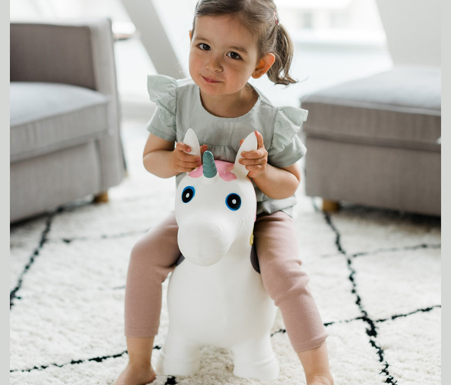 Mädchen sitzt auf Hüpftier »Einhorn« im Wohnzimmer.