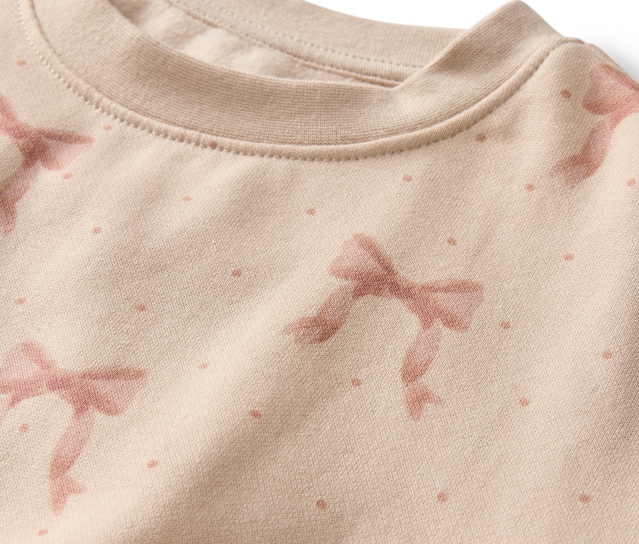 Detailaufnahme eines beigen Sweatshirts mit rosa Schleifen- und Punktmuster.