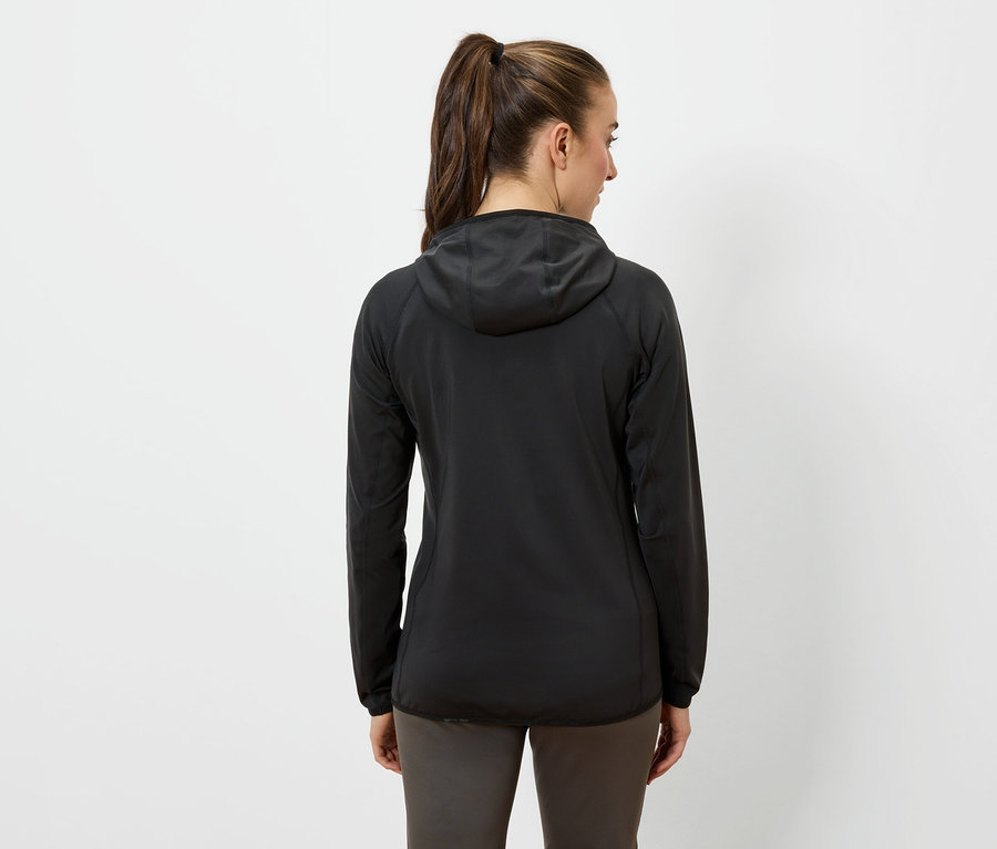 Frau mit dem Rücken zur Kamera trägt eine schwarze Kapuzenjacke und dunkle Hosen.