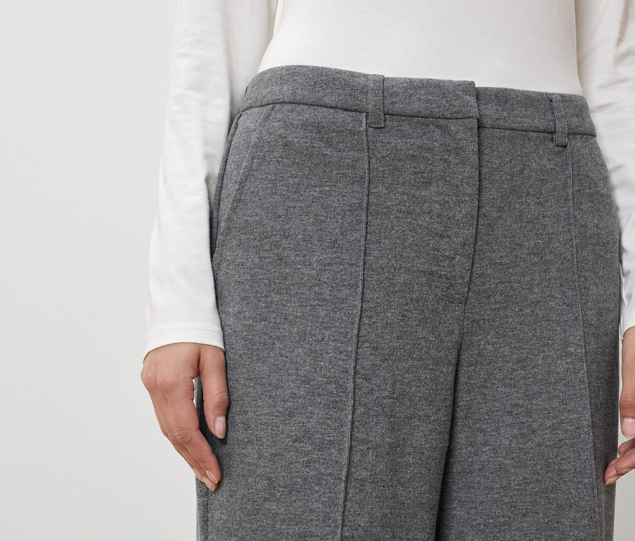 Frau trägt graue Hose und weißes Oberteil.