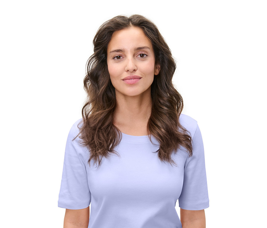 Porträt einer Frau mit braunem, gewelltem Haar und einem hellblauen T-Shirt vor einem weißen Hintergrund.