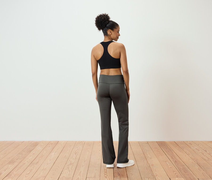 Von hinten ist eine Frau mit hochgesteckten Haaren zu sehen, die einen schwarzen Sport-BH und graue Hosen trägt.