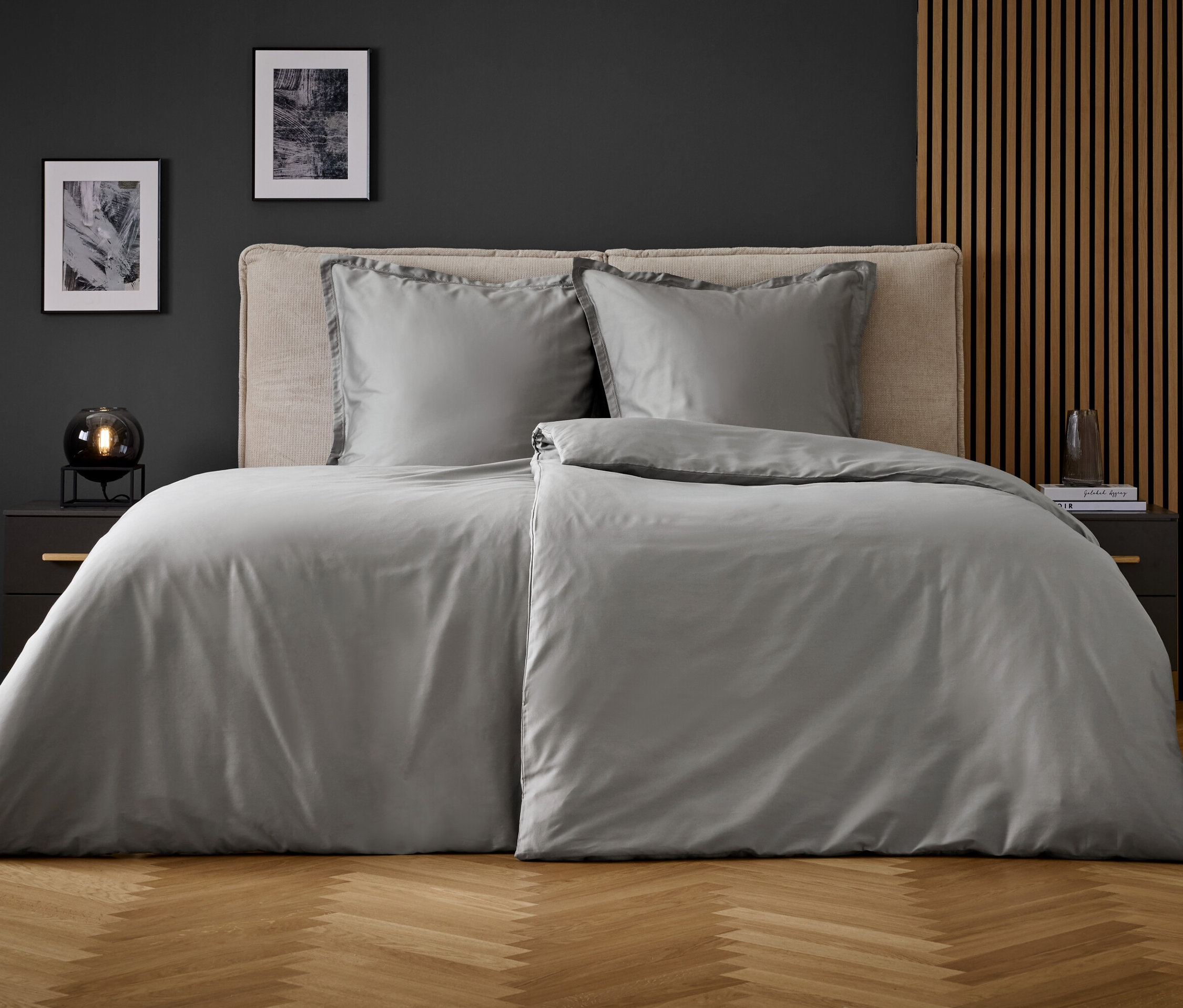 Graue Bettwäsche auf einem Bett mit zwei Kissen und Nachttischen an den Seiten.