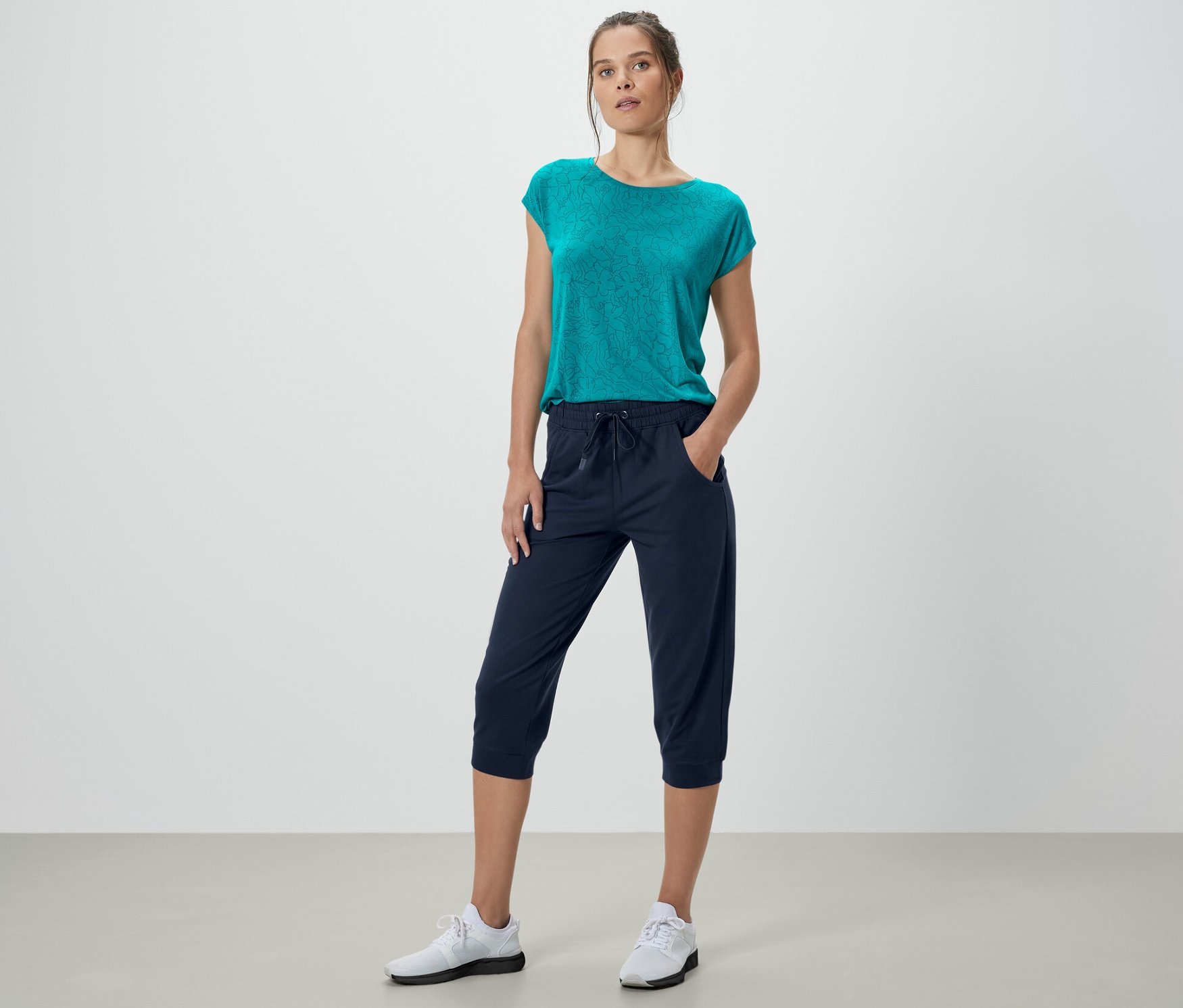 Frau posiert in dunkelblauer 3/4-Sweathose und blaugrünem Oberteil.