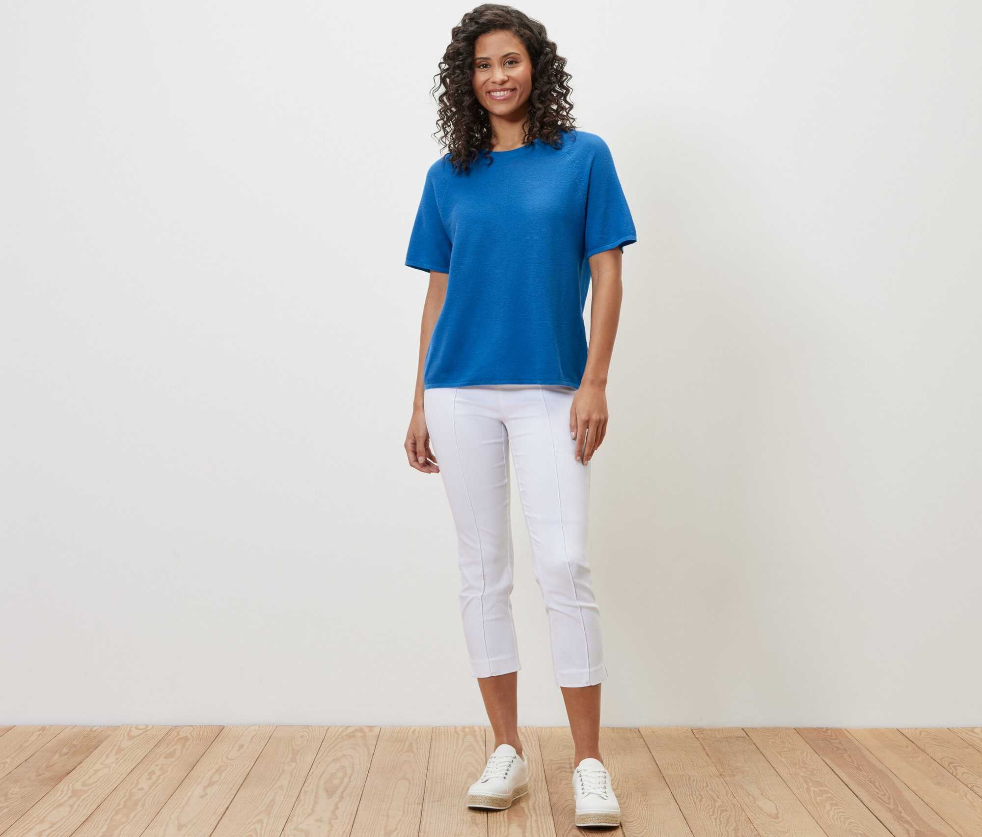Frau trägt ein kobaltblaues Feinstrick-Shirt, weiße Hosen und weiße Turnschuhe.