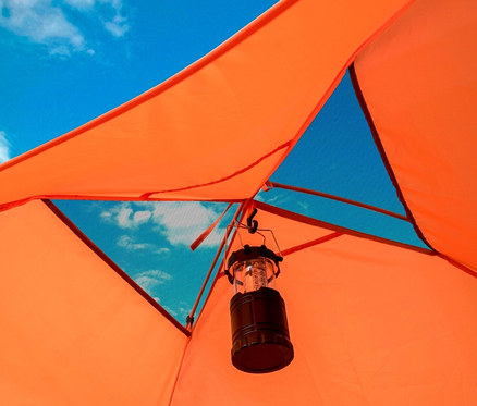 Blick aus dem Inneren eines orangefarbenen Tambu Haika 2-Personen-Kuppelzelts auf blauen Himmel mit Wolken und einer hängenden Laterne.