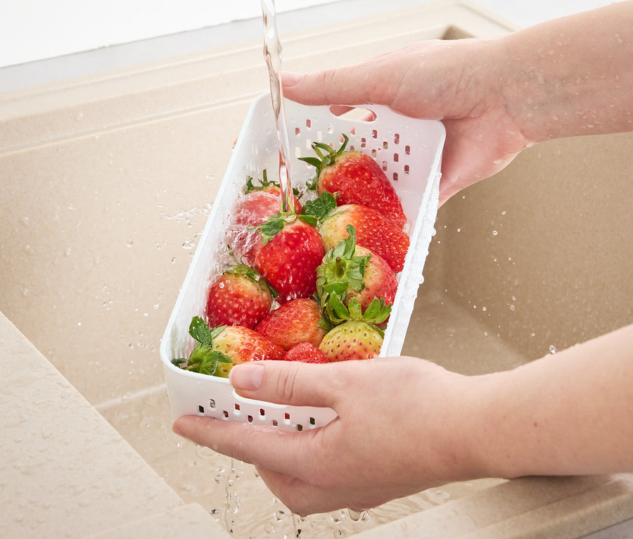 Eine Person wäscht Erdbeeren in einer Frischhaltedose mit Siebeinsatz in der Spüle.