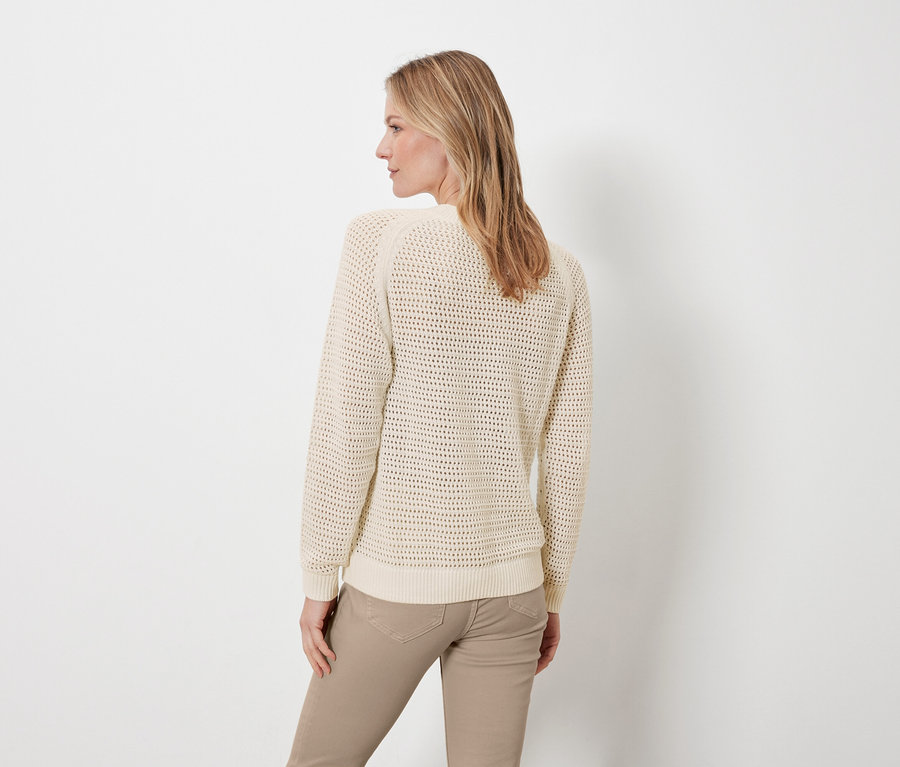 Frau posiert mit dem Rücken zur Kamera und trägt einen cremefarbenen Pullover in Pointellestrick und eine beige Hose.