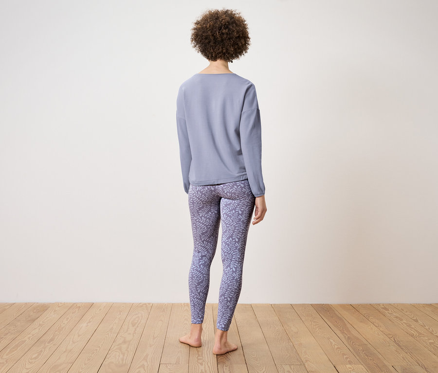 Frau von hinten trägt ein blaues Langarmshirt und gemusterte Leggings.