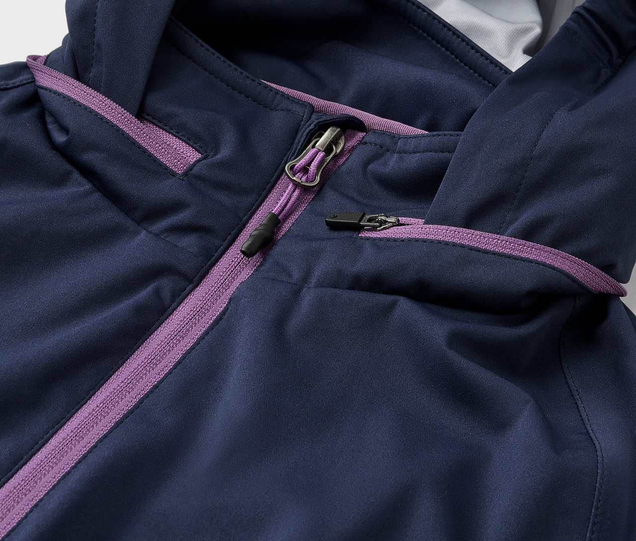 Detailaufnahme einer blauen Rad-Regenjacke mit lilafarbenen Reißverschlüssen.