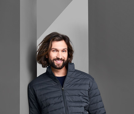 Mann lehnt an Wand und trägt eine Steppjacke.