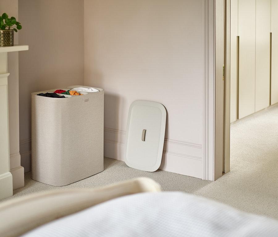 Ein beiger Wäschekorb steht neben einer weißen Wand, der Deckel des Korbs liegt daneben.