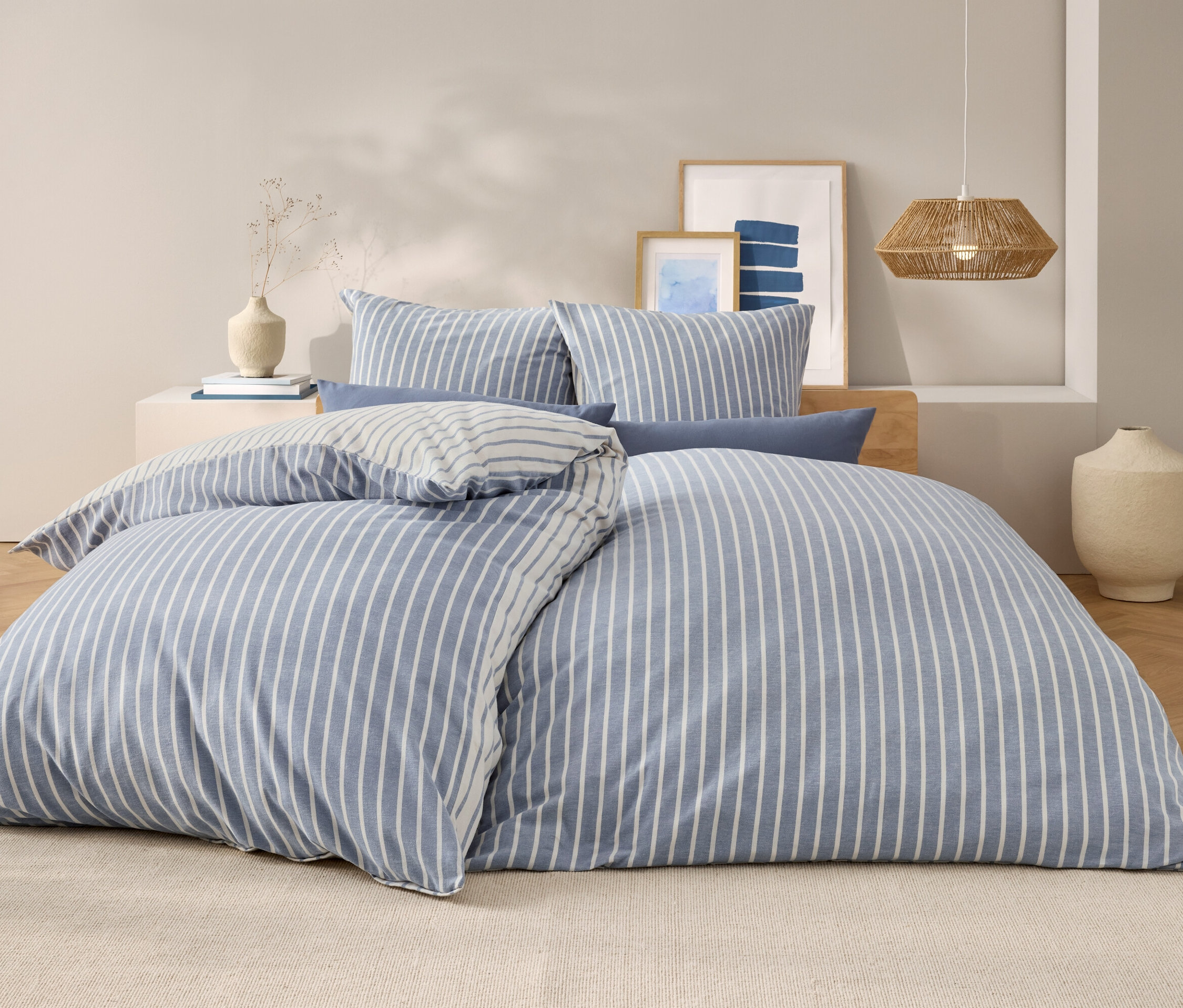 Schlafzimmer mit einem Bett mit blau-weiß gestreifter Bettwäsche, Kissen und Lampe.