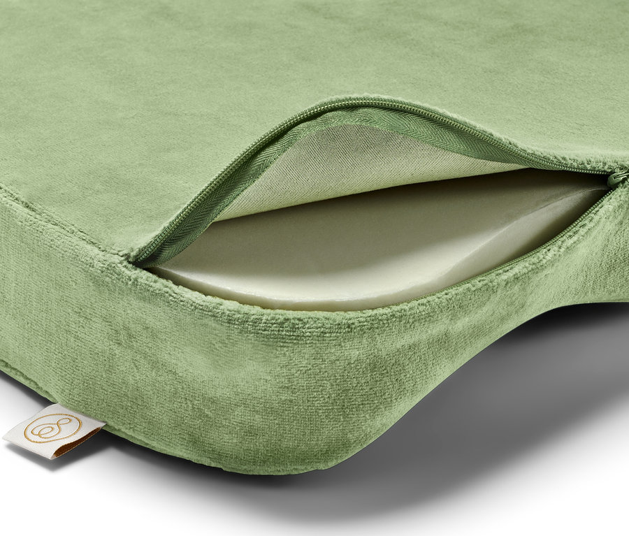 Ein grünes Kissen mit einem Reißverschluss, der das weiße Innere freilegt, und einem Etikett in der linken unteren Ecke.