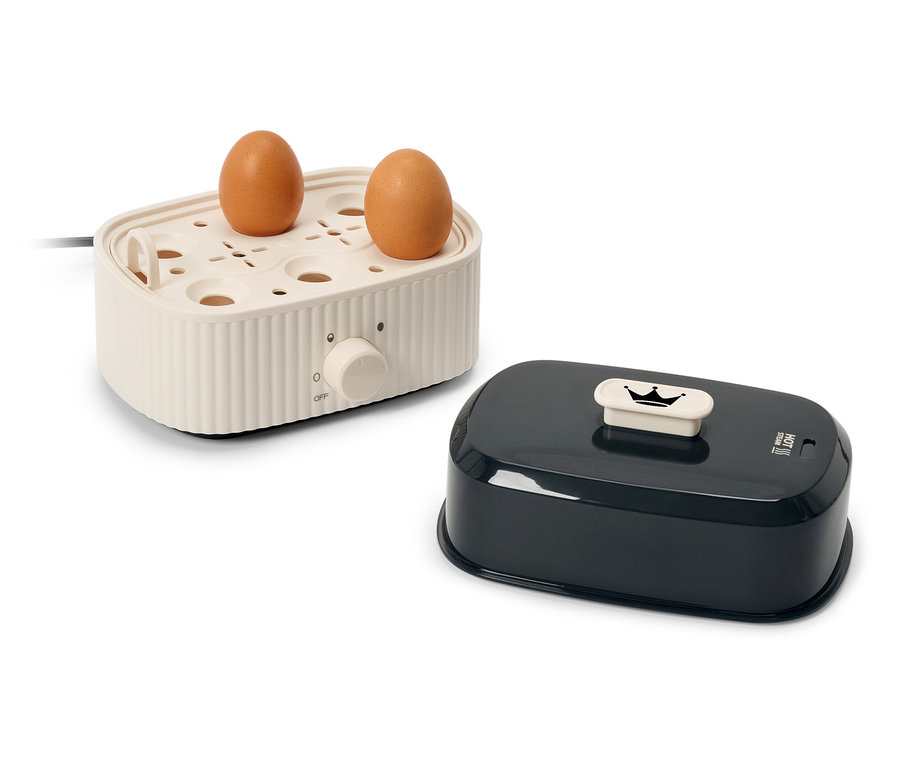 Zwei braune Eier auf einem cremefarbenen elektrischen Eierkocher neben einem schwarzen Deckel.