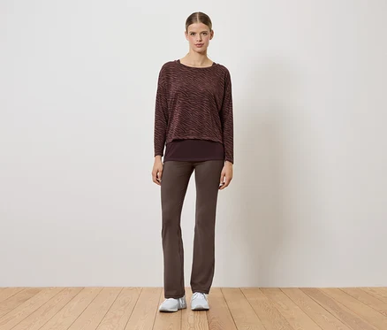 Eine Frau in einem braunen Pullover und braunen Hosen steht auf einem Holzboden.