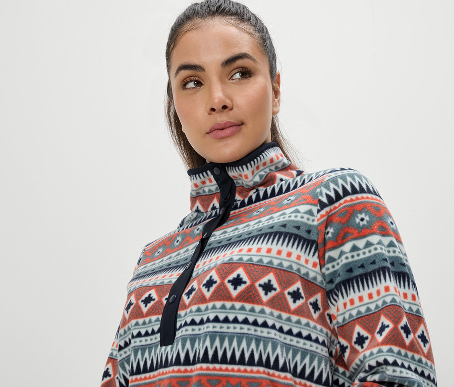 Porträt einer Frau mit braunen Haaren, die ein bunt gemustertes Fleece-Oberteil mit geometrischem Muster trägt.