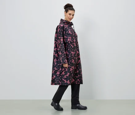 Frau trägt einen langen Regenmantel mit Blumenmuster in Pink und Schwarz, dazu schwarze Hose und Stiefel.