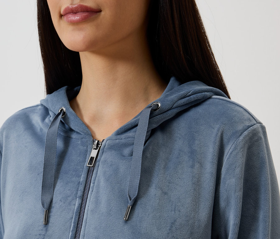 Nahaufnahme einer Frau mit langem, dunklem Haar, die einen blauen Kapuzenpullover mit Reißverschluss trägt.