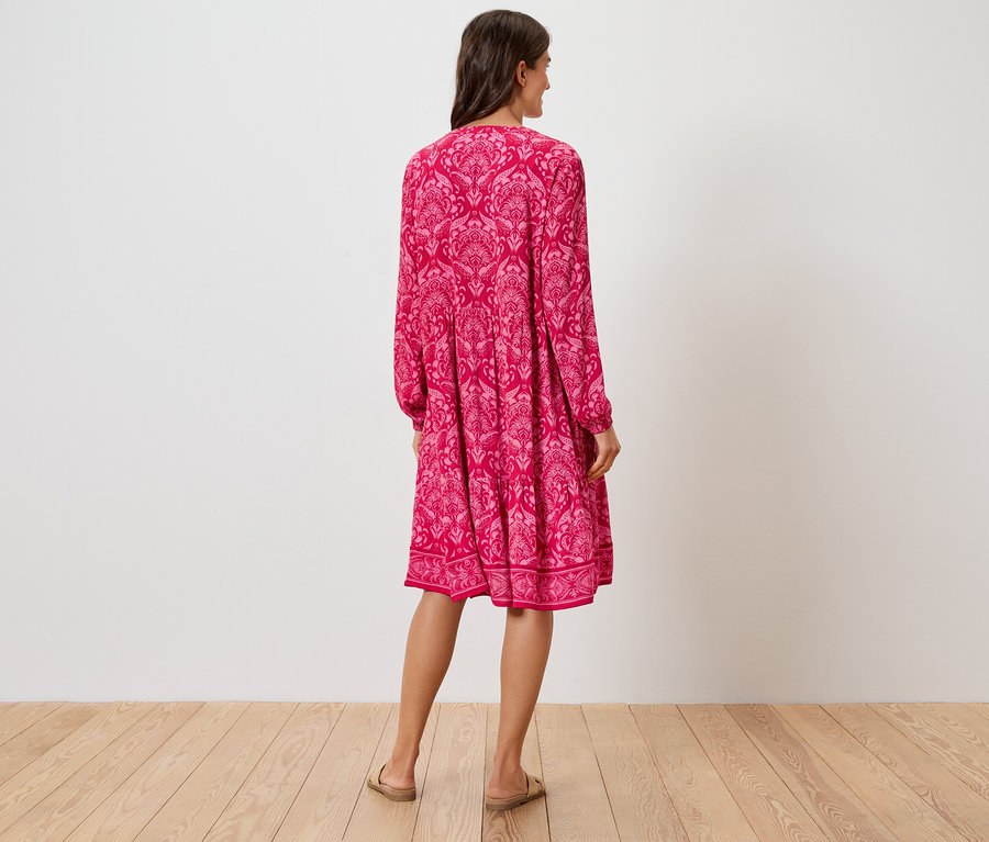 Rückansicht einer Frau in einem knielangen, pinkfarbenen Kleid mit Blumenmuster und Sandalen.