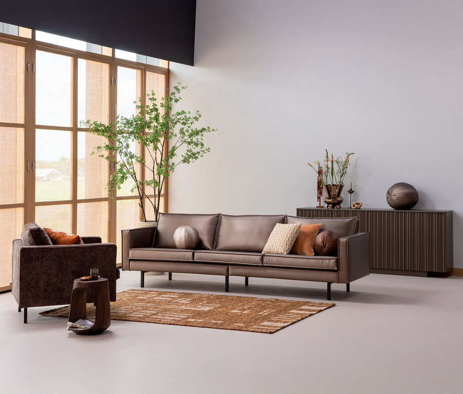 Wohnzimmer mit braunem Sofa, Sessel, Holztisch und einem handgewobenen braunen »Ian« Teppich (170 x 240 cm).