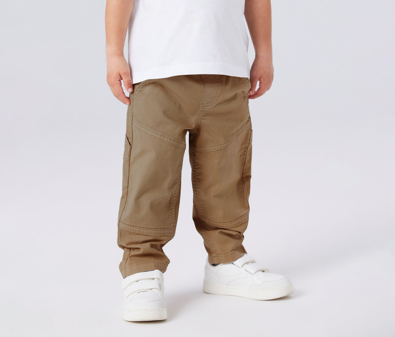 Kind trägt ein weißes T-Shirt, NAME IT Kinder-Twillhose und weiße Turnschuhe.