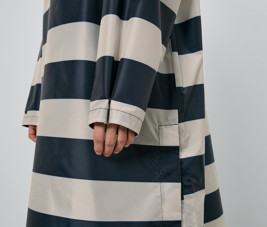 Nahaufnahme einer Person, die einen gestreiften Regenmantel in Marineblau und Beige trägt.