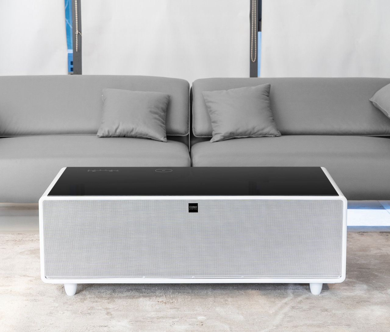 Weißer Caso Sound & Cool Tisch mit schwarzer Glasplatte steht vor einem grauen Sofa.
