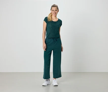 Frau trägt ein grünes T-Shirt und eine grüne Hose und weiße Turnschuhe.