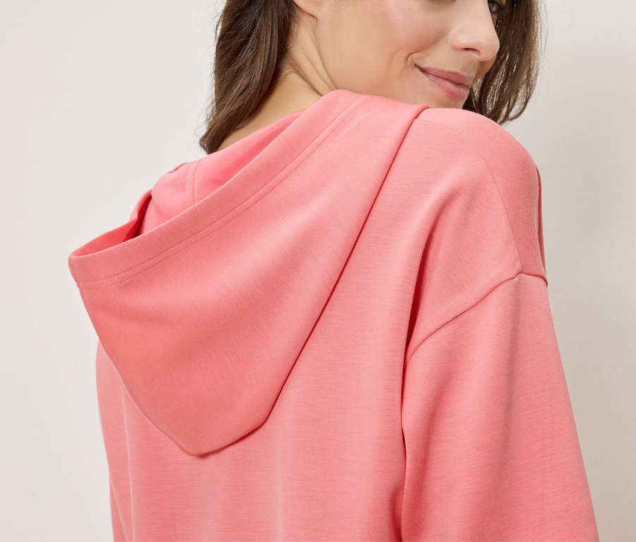 Frau trägt einen lachsfarbenen Hoodie, von der Seite gesehen.