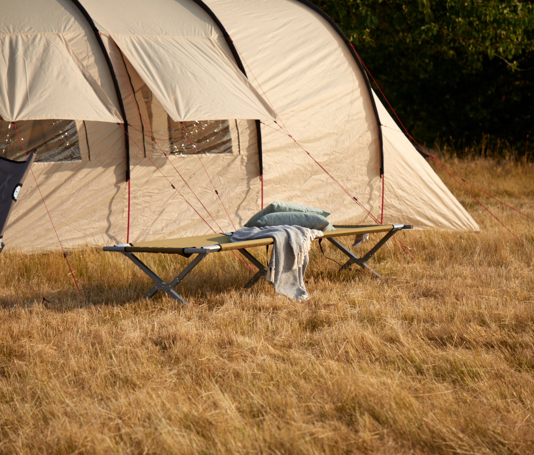 Eine Grand Canyon Campingliege »Topaz« (190 oder 210 cm) mit Kissen und Decke steht vor einem Zelt auf einer Wiese.
