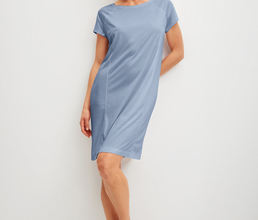 Frau lehnt an einer Wand und trägt ein blaues Kleid.
