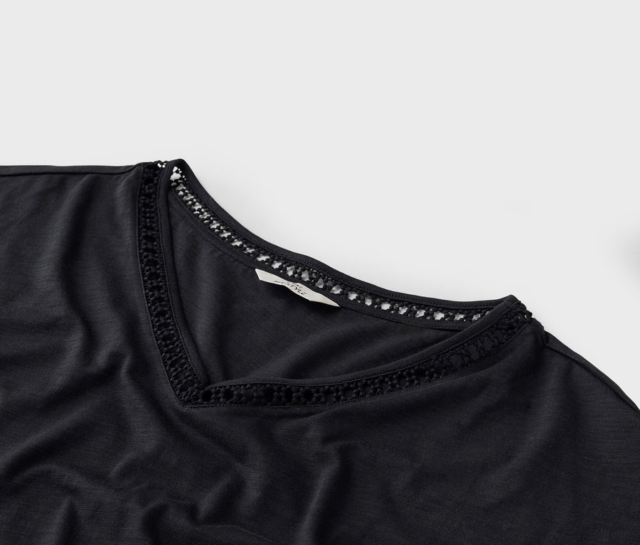 Nahaufnahme eines schwarzen T-Shirts mit V-Ausschnitt und Häkeldetails am Ausschnitt.