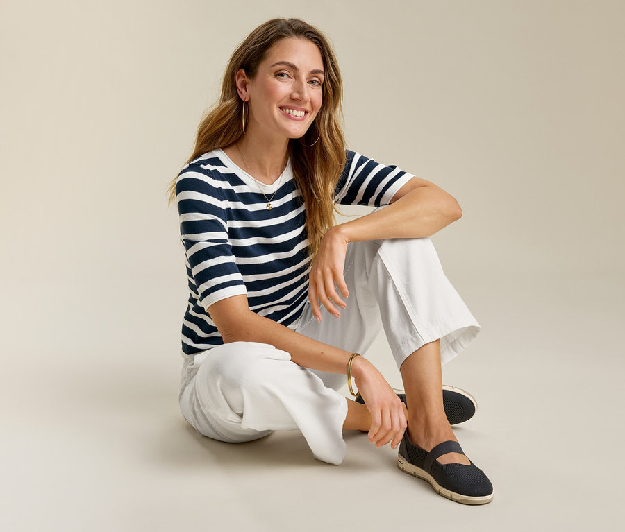 Frau sitzt mit Wide-Komfort-Jeans, blau-weiß gestreiftem Shirt und dunklen Schuhen auf dem Boden.