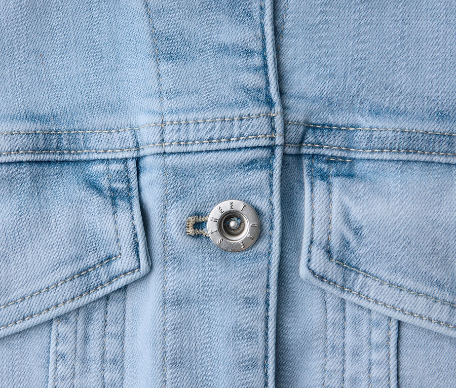 Nahaufnahme einer hellblauen Jeansjacke mit silbernen Knöpfen, Kragen und Taschen.