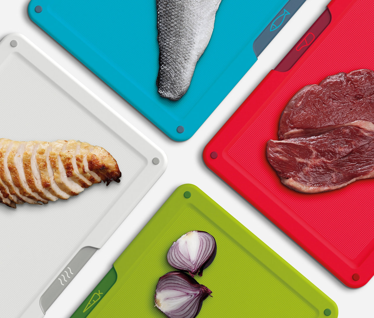 Verschiedene Lebensmittel liegen auf farbigen Schneidebrettern: Fisch auf Blau, Rindfleisch auf Rot, Zwiebeln auf Grün und Hähnchen auf Weiß.