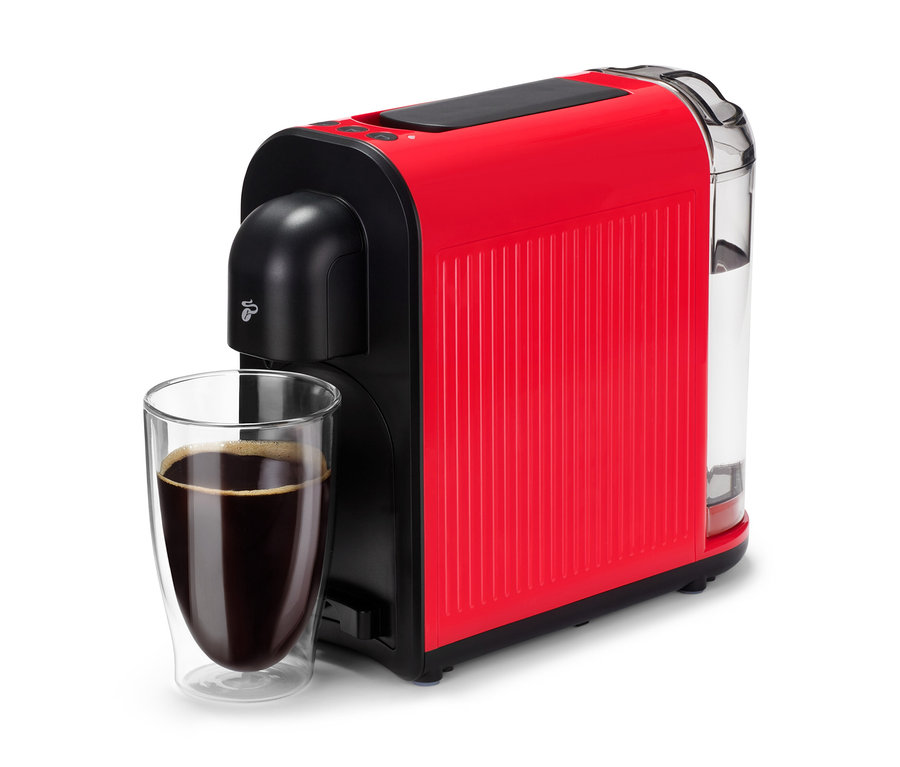 Eine rote Cafissimo now red Kaffeemaschine steht neben einem Glas mit dunklem Kaffee.