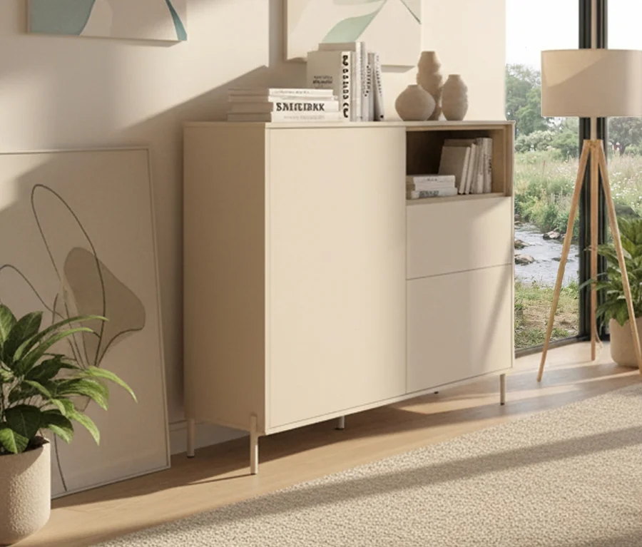 Ein »Hygge« Highboard mit 2 Türen in Kaschmir-Weiß steht im Raum, dekoriert mit Büchern und Vasen. Eine Zimmerpflanze steht daneben.