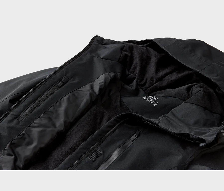 Nahaufnahme einer schwarzen Jacke mit glatter Außenhülle und weichem Fleece-Innenfutter. Schwarze Reißverschlüsse und ein weißes "ACTIVE"-Etikett sind sichtbar.