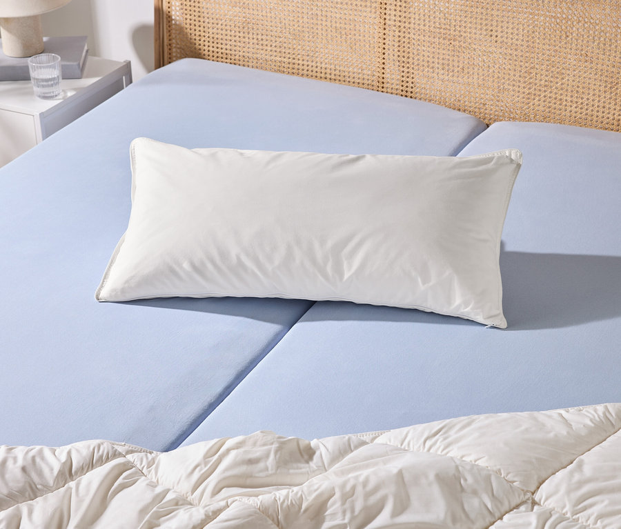 Ein Bett mit hellblauem Spannbettlaken, einem weißen Kissen und einer weißen Bettdecke. Daneben steht ein weißer Nachttisch mit Lampe und Wasserglas.
