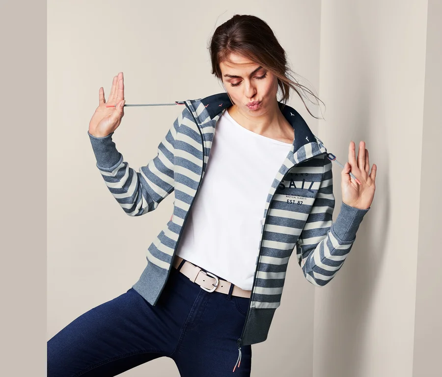 Frau posiert in blauen Jeans und einer gestreiften Sweatjacke mit Kapuze.