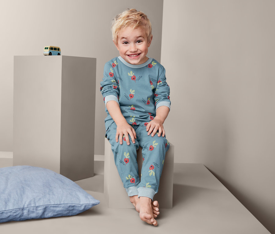 Ein Junge sitzt und trägt einen Pyjama mit Radieschen-Muster.