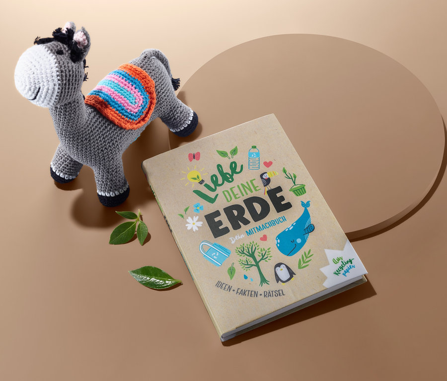Brauner Tisch mit dem Buch "Liebe deine Erde" und einem gestrickten Esel Spielzeug.