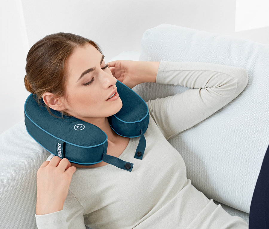 Frau entspannt mit einem Nackenkissen mit Vibrationsmassage auf der Couch.