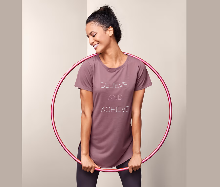 Frau hält Hula-Hoop-Reifen und trägt ein Sportshirt mit Schriftzug.