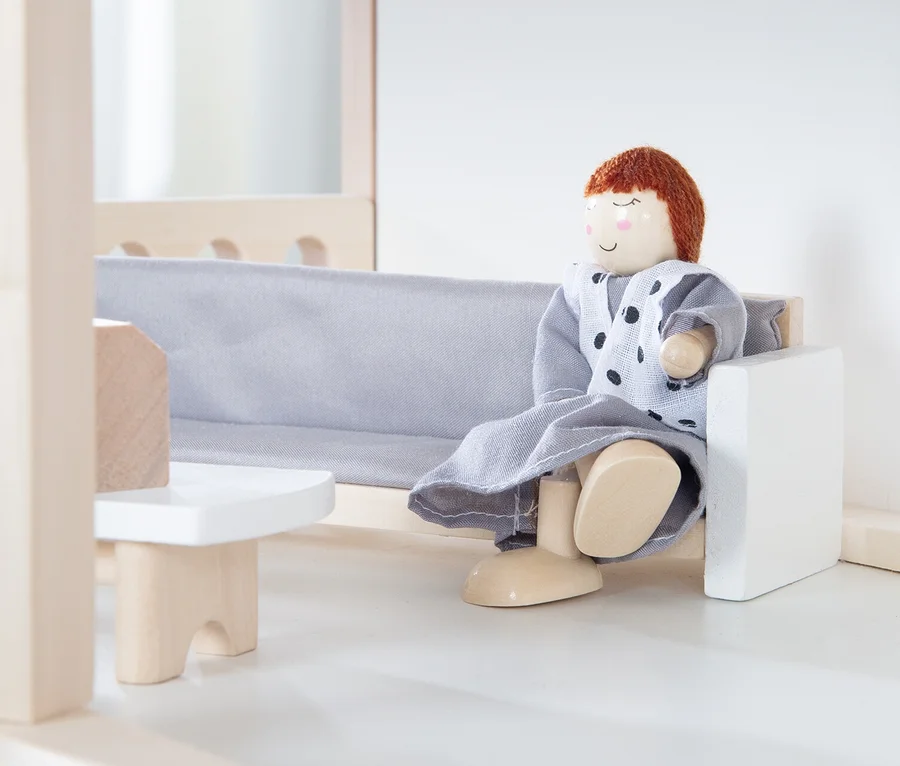 Puppe sitzt auf einem grauen Sofa im roba Puppenhaus inkl. Zubehör.