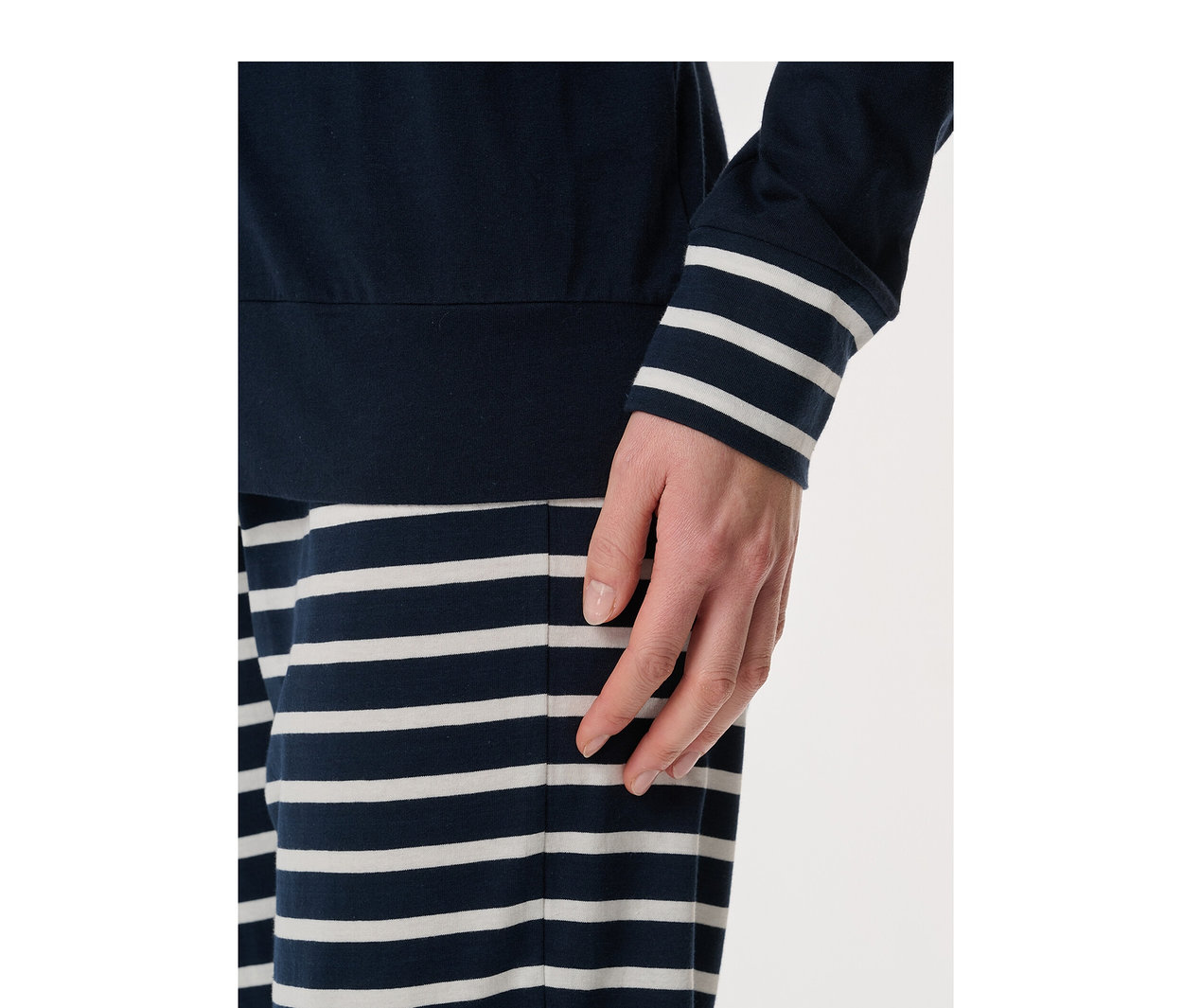 Person trägt ein SCHIESSER Pyjama-Set: dunkelblaues Langarmshirt mit gestreiften Ärmelbündchen und dunkelblau-weiß gestreifte Hose. Eine Hand ruht auf der Hüfte.