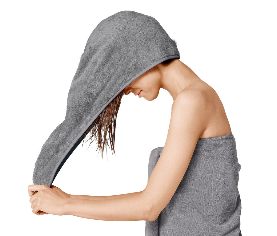 Frau setzt ein graues Turban-Handtuch auf das nasse Haar und ist in ein Handtuch gewickelt.