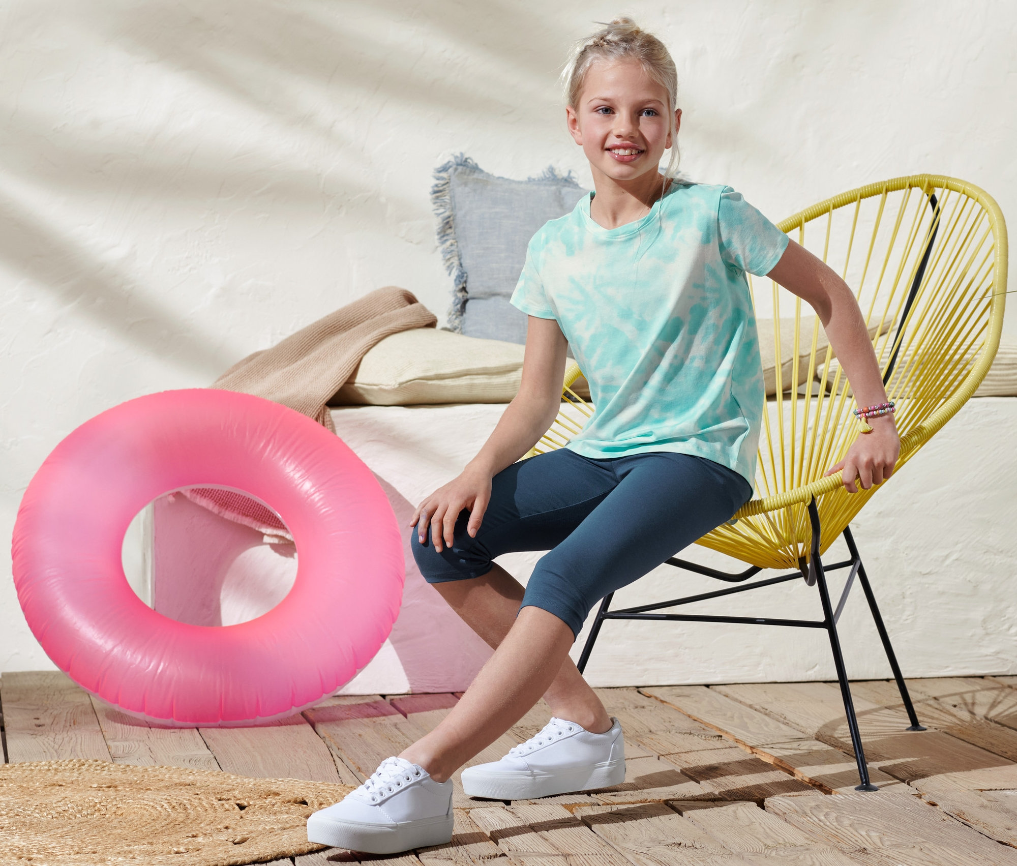 Mädchen sitzt auf gelbem Stuhl und trägt 2 Leggings in 3/4-Länge aus Bio-Baumwolle.